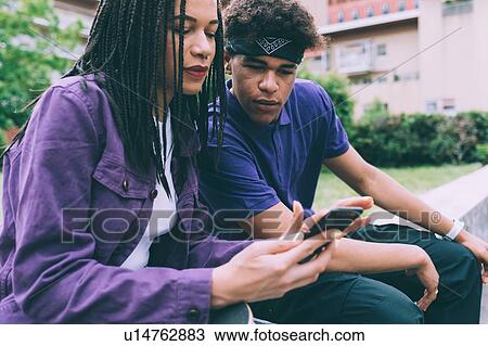 Stock Image - Brother and sister sharing text on mobile phone, Milan, Italy. Fotosearch