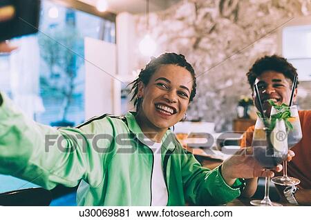 Stock Image - Brother and sister taking selfie in bar. Fotosearch