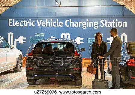 Stock Photograph - Businessman and businesswoman at electric vehicle charging station, Manchester, UK. Fotosearch