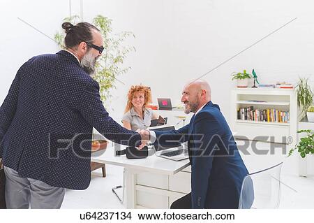 Picture - Businessman and client shaking hands at office desk. Fotosearch