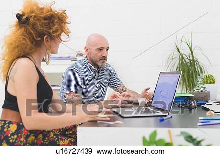 Stock Photo - Businessman and woman looking at laptop in office. Fotosearch