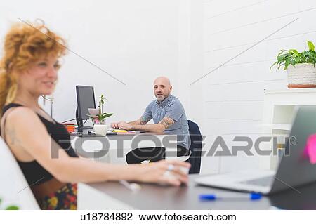 Stock Image - Businessman and woman using laptops in office. Fotosearch