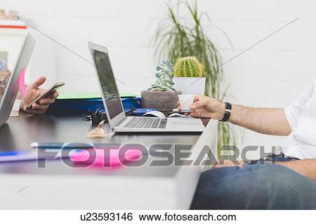 Stock Photograph - Businessman drinking water at office desk, cropped. Fotosearch