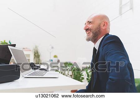 Businessman laughing at office desk View Large Photo Image Stock Image - Businessman laughing at office desk. Fotosearch