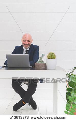 Businessman laughing while looking at laptop on office desk View Large Photo Image Stock Image - Businessman laughing while looking at laptop on office desk. Fotosearch