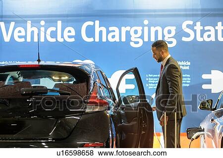 Businessman opens door of electric vehicle car at electric vehicle charging station, Manchester, UK View Large Photo Image Stock Photo - Businessman opens door of electric vehicle car at electric vehicle charging station, Manchester, UK. Fotosearch