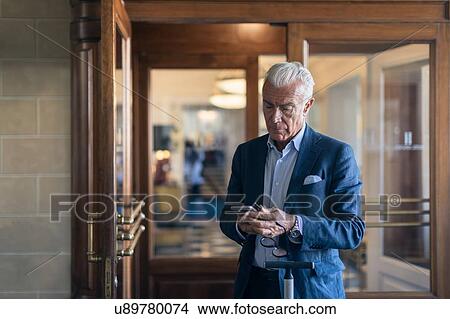 Picture - Businessman reading text message in front of office. Fotosearch