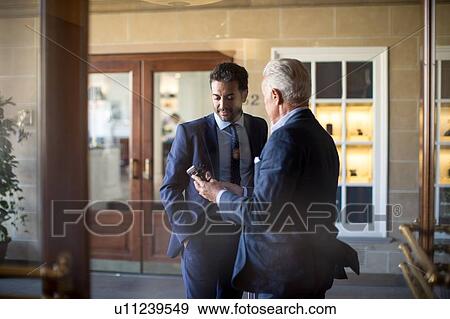 Businessman showing text message to colleague in front of office View Large Photo Image Stock Photo - Businessman showing text message to colleague in front of office. Fotosearch