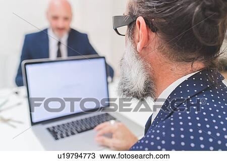 Stock Image - Businessman using laptop at office desk, over shoulder view. Fotosearch
