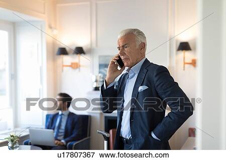 Businessman using smartphone, colleague using laptop in office View Large Photo Image Stock Photo - Businessman using smartphone, colleague using laptop in office. Fotosearch