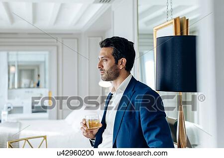 Stock Image - Businessman with iced drink, deep in thoughts in suite. Fotosearch