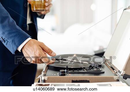 Stock Photo - Businessman with iced drink, playing turntable in suite. Fotosearch
