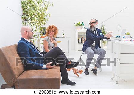Stock Photography - Businessmen and woman having discussion at meeting on office sofa. Fotosearch