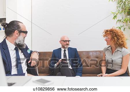 Stock Photograph - Businessmen and woman meeting on office sofa. Fotosearch