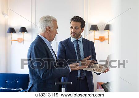 Stock Photo - Businessmen talking and using laptop in office. Fotosearch