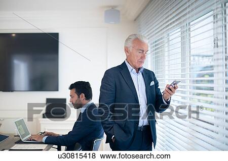 Stock Photo - Businessmen using smartphone and laptop in office. Fotosearch