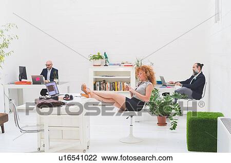 Businessmen working at office desks and businesswoman with her feet up View Large Photo Image Stock Image - Businessmen working at office desks and businesswoman with her feet up. Fotosearch