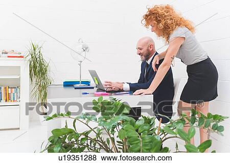 Stock Photo - Businesswoman and man looking at laptop on office desk. Fotosearch