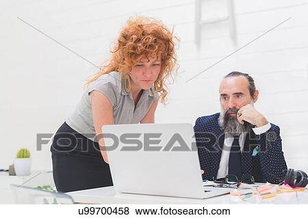 Stock Photo - Businesswoman and man looking at laptop on office desk. Fotosearch