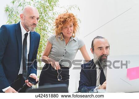 Stock Image - Businesswoman and men looking at laptop on office desk. Fotosearch