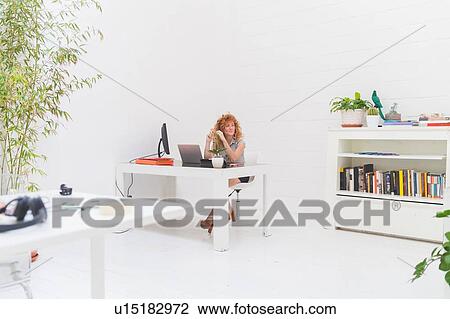Stock Image - Businesswoman gazing from office desk. Fotosearch