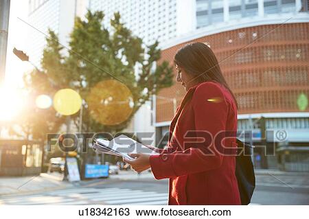 Stock Image - Businesswoman reading newspapers in city, Seoul, South Korea. Fotosearch