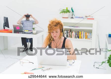 Businesswoman typing on laptop at office desk while listening to headphones View Large Photo Image Picture - Businesswoman typing on laptop at office desk while listening to headphones. Fotosearch