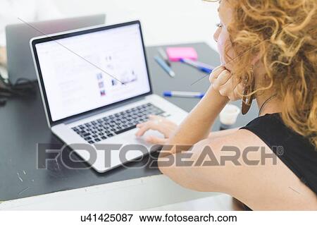 Businesswoman typing on laptop at office desk, over shoulder view View Large Photo Image Stock Photo - Businesswoman typing on laptop at office desk, over shoulder view. Fotosearch