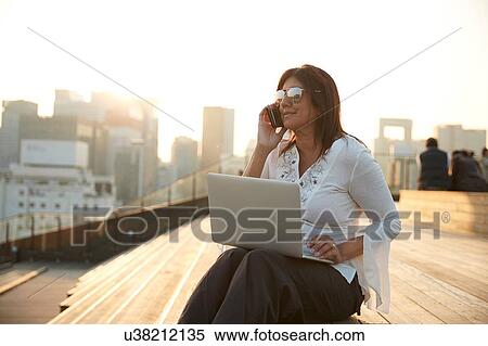 Stock Photography - Businesswoman using laptop and smartphone on steps, Seoul, South Korea. Fotosearch