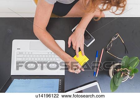 Stock Image - Businesswoman writing sticky notes on office desk, overhead view. Fotosearch