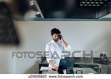Chef using laptop and cellphone in kitchen View Large Photo Image Stock Image - Chef using laptop and cellphone in kitchen. Fotosearch