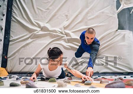 Stock Image - Climber guiding friend on climbing wall. Fotosearch