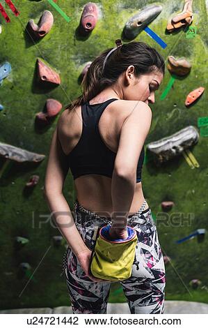 Stock Image - Climber reaching for chalk bag, climbing wall in background. Fotosearch