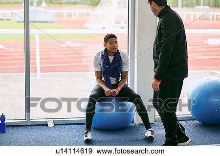 Stock Photo - Coach and runner speaking in indoor running track. Fotosearch