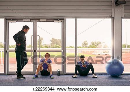 Picture - Coach and runners speaking in indoor running track. Fotosearch