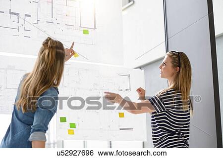 Stock Photograph - Colleagues discussing plans on glass wall. Fotosearch