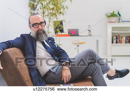 Stock Photograph - Cool hipster businessman sitting on office sofa, portrait. Fotosearch