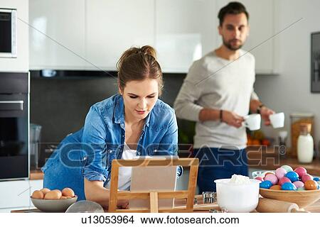 Picture - Couple drinking coffee and using digital tablet in kitchen. Fotosearch