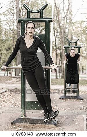 Stock Image - Couple exercising in public outdoor gym. Fotosearch