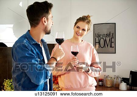 Stock Image - Couple talking and drinking red wine in kitchen. Fotosearch