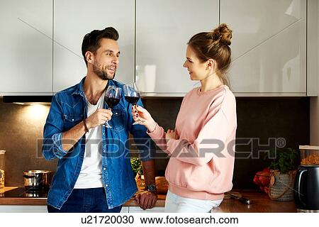 Stock Image - Couple talking and drinking red wine in kitchen. Fotosearch