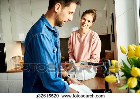 Stock Image - Couple talking and washing up in kitchen. Fotosearch
