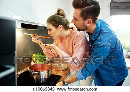 Stock Image - Couple tasting tomato soup in kitchen. Fotosearch