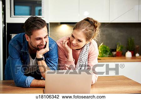 Stock Image - Couple using laptop in kitchen. Fotosearch