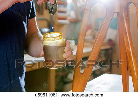 Stock Image - Craftsman polishing wooden stool with oil finish. Fotosearch