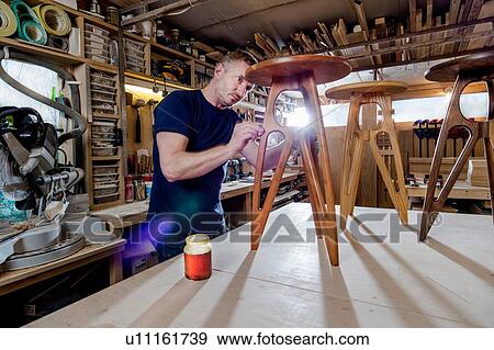 Stock Photo - Craftsman polishing wooden stool with oil finish. Fotosearch