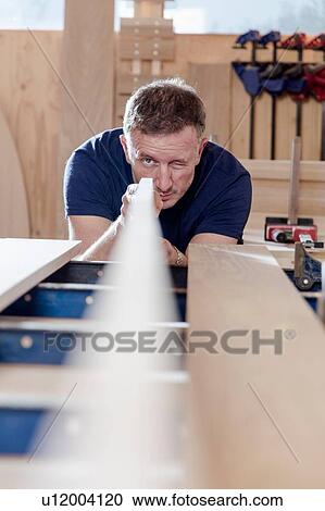 Stock Image - Craftsman preparing planks of wood in workshop. Fotosearch