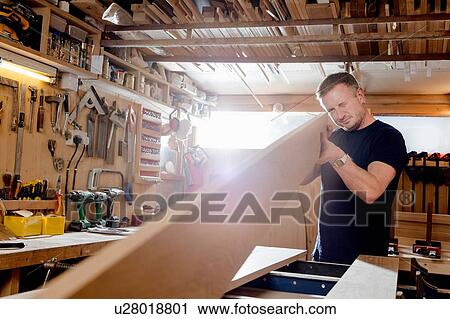 Stock Image - Craftsman preparing planks of wood in workshop. Fotosearch