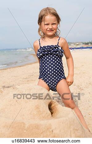 Stock Image - Cute girl building sandcastle on beach in spotted swimming costume, portrait, Castellammare del Golfo, Sicily, Italy. Fotosearch