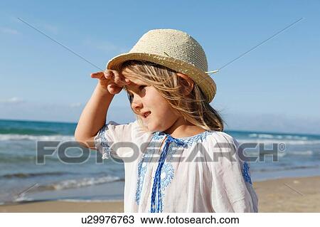 Stock Image - Cute girl on beach shielding her eyes, Castellammare del Golfo, Sicily, Italy. Fotosearch